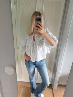 Vit blommig blus från Gina Tricot  - Söt och luftig vit blus med ljusblått blommönster. Blusen har trekvartsärmar med volangkant, rundad halsringning och knytband framtill. Passformen är lös och flowy, perfekt till jeans eller kjol. Endast använd ett fåtal gånger 