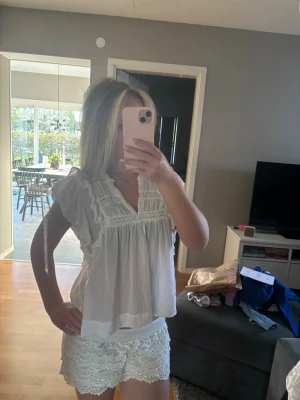 Vit blus med spetsdetaljer - Säljer en vit blus, använd fåtal gånger och fråga ifall ni undrar något!💗 Söt vit blus med volang och spetsdetaljer vid axlar och bröst. Blusen har v-ringning och är ärmlös med en luftig och lös passform. Perfekt för varma dagar och ger en romantisk vibe till din outfit.