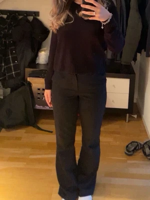 Svarta utsvängda kostymbyxor - Säljer ett par svarta kostymbyxor med utsvängda ben och hög midja. Byxorna har en klassisk look och är perfekta för en stilren outfit. Materialet ser ut att vara en mjuk och följsam blandning, vilket ger en snygg passform.