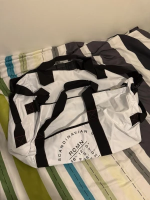 Vit duffelbag med svarta detaljer ( RaceMarine) - Säljer en vit duffelbag med svarta remmar och detaljer. Väskan har tryckt text på sidan och flera bärhandtag samt axelrem. Perfekt för gymmet eller resan, rymmer mycket och har en sportig look. Materialet är slitstarkt syntet. One size , märke: Racemarine