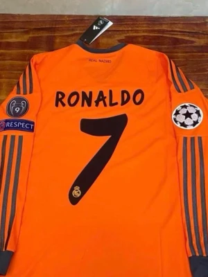 Real Madrid Ronaldo matchtröja orange - Säljer en långärmad Real Madrid matchtröja i orange med svarta detaljer, nummer 7 och Ronaldo på ryggen. Tröjan har Champions League-patchar på ärmarna, Fly Emirates-tryck på bröstet och klassiska Adidas-ränder längs ärmarna. 