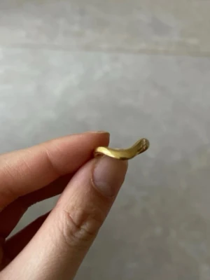 Guldfärgad vågig ring - Säljer en stilren guldfärgad ring med vågig form. Ringen är öppen baktill vilket gör den justerbar i storlek. Perfekt för dig som gillar minimalistiska smycken med en twist.