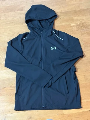 Svart hoodie - Cool svart hoodie  med dragkedja och huva. Logotypen syns på bröstet och stort tryck på ryggen. Materialet är mjukt och stretchigt, perfekt för träning eller chill. Reflekterande detaljer på axlarna ger extra stil.
