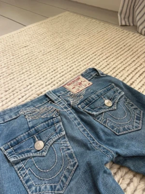 Blå True Religion jeans med brodyr - Snygga true religion jeans i storlek w24. Säljer då de inte passade mig (ej mina bilder) superfint skick med broderade vingar på bakfickorna. De är bootcut och low waist, de är även någorlunda uppsydda av tidigare ägare men går lätt att tas ned 💗