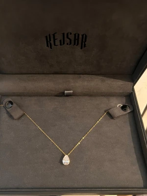 18k guldpläterat  halsband med droppformad sten - 18k guldplaterat halsband med droppformat kristall från Kejsar. Elegant halsband som ger ett stilrent och tidlöst utseende. Passar perfekt till både vardags och festliga tillfällen, går enkelt att matcha med andra smycken och att ha den sjalv. Droppformade hänget med en klar sten ger ett elegant intryck och går ihop med alla outfits. Halsbandet säljs i nyskick och har aldrig använts. Ett fint smycke att ge bort i present eller att unna sig sjalv! 