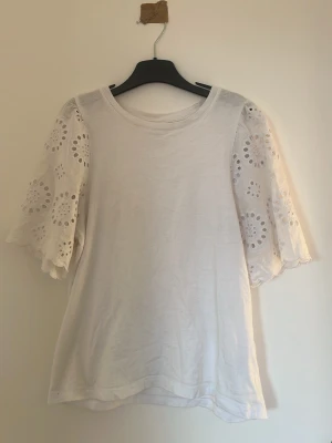 Vit topp med broderade ärmar H&M - Söt vit topp från H&M med vida, korta ärmar i broderad spets i storlek XS.