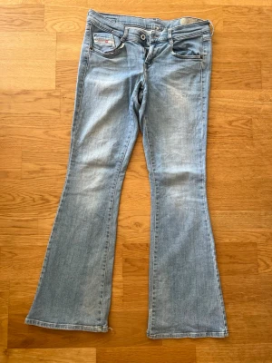 Ljusblå bootcut jeans från Diesel - Snygga ljusblå bootcut jeans från Diesel med klassisk femficksmodell och slitna detaljer vid bensluten. Jeansen har en avslappnad passform och är tillverkade i mjukt denimtyg. Perfekta för en casual och trendig look. Storlek 29 men passar som 36-38