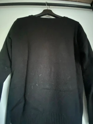 Svart stickad tröja med rund hals - En enkel svart stickad tröja med rund halsringning och långa ärmar. Tröjan har ribbstickad nederkant och är tillverkad i ett mjukt material som passar perfekt till många olika stilar.