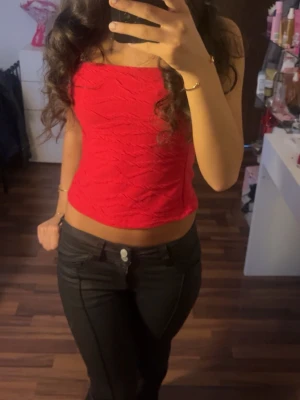 Röd tube top - Säljer en röd croppad topp med fyrkantig ringning och strukturerad yta. Toppen är ärmlös och har en tajt passform som framhäver midjan. Perfekt för dig som vill ha en enkel men snygg topp till din outfit.