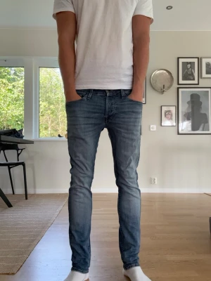 Blåa Jack & Jones glenn - Säljer ett par blå slim fit jeans med klassisk femficksdesign och normalhög midja. Jeansen har en snygg tvättad look och smal passform hela vägen ner. Perfekta för dig som gillar en modern och enkel stil.