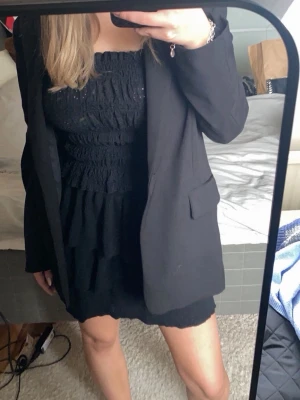 Svart linnetopp - Supersöt svart linnetopp med smockad resår över hela toppen och smala axelband. Toppen är croppad och har en lätt volangkant nertill. Perfekt att styla med kavaj eller kjol för en trendig look.