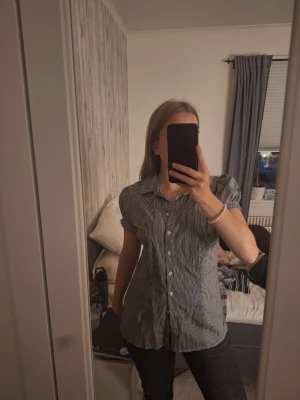 Randig kortärmad skjorta - Snygg skjorta med smala svarta och vita ränder. Modellen har puffiga korta ärmar och klassisk krage. Knäpps framtill med vita knappar. Perfekt till jeans eller kjol för en avslappnad men stilsäker look.