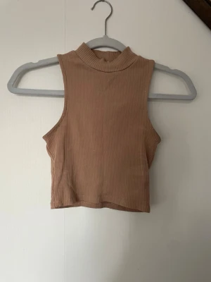 Beige/rosa ribbad croppad linnetopp - Säljer en beige/rosa croppad linnetopp med hög hals och ribbad struktur. Toppen är ärmlös och har en clean och enkel design.