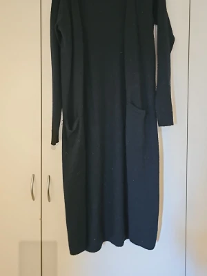 Svart lång stickad klänning Vila - Svart långklänning från Vila i mjukt stickat material. Klänningen har lång ärm och två stora fickor framtill. Enkel och clean design som är lätt att styla med accessoarer.