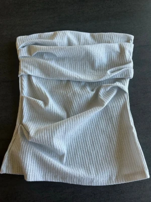 Silvrig/grå ribbad tubtopp - Säljer en stilren ljusgrå ribbad tubtopp. Toppen är axelbandslös och har en mjuk, stretchig passform som sitter snyggt på kroppen. Perfekt att matcha med jeans eller kjol för en trendig look.