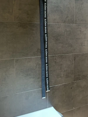 Svart textbälte från Björn Borg och mörkblått peak performance  - Snyggt svart bälte från Björn Borg med tydlig vit logotyptext längs hela bandet. Bältet har en metallspänne med graverad logga och texten 'BORG'. Perfekt för att ge din outfit en sportig touch.snyggt mörkblått bälte från peak pearformace 