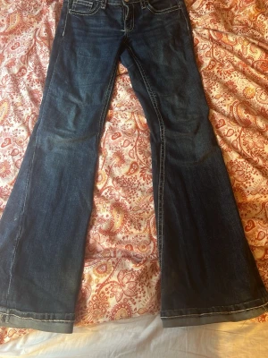 Mörkblå bootcut jeans - Säljer ett par mörkblå bootcut jeans med kontrastsömmar och klassisk femficksmodell. Jeansen har utsvängda ben och är tillverkade i ett mjukt denimtyg som ger en snygg vintagekänsla. Perfekta för dig som gillar retrostil och vill ha ett par jeans med skön passform.