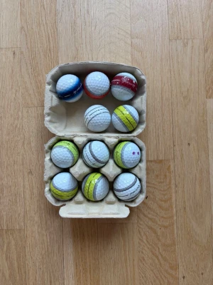 11 taylormade stripe a klass - Säljer ett set med 11 golfbollar i olika färger och mönster, förvarade i en äggkartong. Bollarna har detaljer i vitt, gult, blått och rött samt svarta linjer. Perfekt för dig som vill ha lite extra stil på golfbanan. Och funkar även som perfekta bollar 