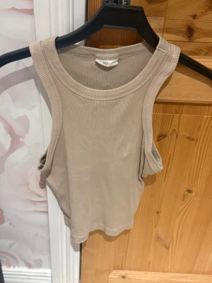 Beige ribbad linnetopp - Säljer en enkel och stilren beige linnetopp i ribbat material. Toppen är ärmlös med breda axelband och har en klassisk rund halsringning. Perfekt att matcha med jeans eller kjol för en avslappnad look.