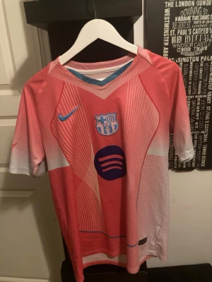 Barcelona rosa matchtröja Nike - Säljer en rosa Barcelona matchtröja med vita och blå detaljer. Tröjan har klubbmärke och Nike-logga på bröstet samt Spotify-logga. På ryggen står det 'Lamine Yamal' och nummer 10 i blått. Perfekt för dig som älskar fotboll och vill sticka ut på planen.