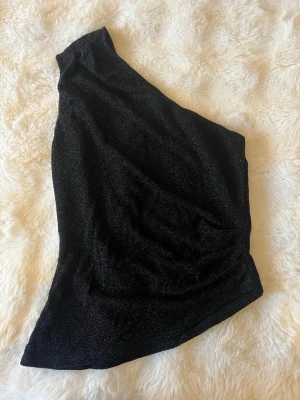 Svart glittrig oneshoulder topp - Snygg svart topp med glittrigt tyg och oneshoulder-design, köpt på Gina och är snygg passform på. 