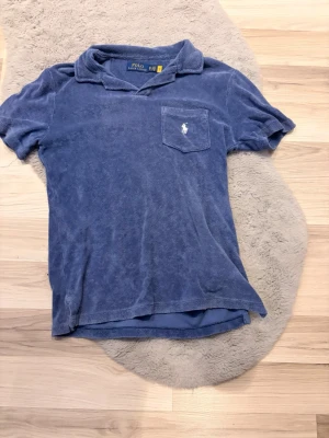 Blå frottéskjorta från Polo Ralph Lauren - Säljer en blå kortärmad skjorta från Polo Ralph Lauren i mjuk frotté. Skjortan har klassisk krage, bröstficka med broderad logga och avslappnad passform. Perfekt för en chill och sportig stil.