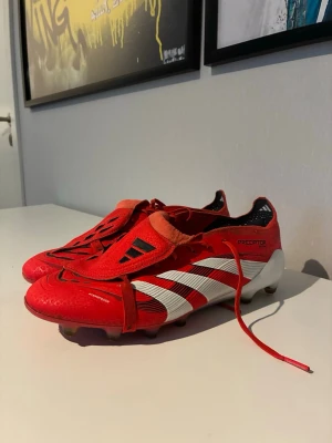 Adidas Predator röda fotbollsskor - Säljer ett par ikoniska Adidas Predator fotbollsskor i rött med vita och svarta detaljer. Skorna har klassisk snörning, gummidobbar och tydliga Predator-loggor. Perfekta för dig som vill sticka ut på planen med stil och grym kontroll.HÖR AV ER VID FRÅGOR!