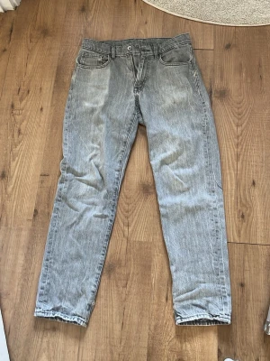Grå raka jeans med fem fickor - Säljer ett par grå jeans med rak passform och klassisk femficksdesign. Jeansen har normal midja, bälteshällor och dragkedjegylf. Materialet är denim i bomull och färgen är ljusgrå med tvättad look. Perfekta för en avslappnad stil.