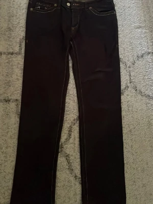 Mörkblå raka jeans från true Religion - Snygga mörkblå jeans från Religion med raka ben och kontrastsömmar. Klassisk femficksmodell och detaljerade metallknappar framtill. Jeansen har en tidlös look och passar perfekt till en avslappnad stil.