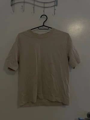 Beige basic t-shirt från Gina Tricot - En enkel och stilren beige t-shirt från Gina Tricot, basically basics-kollektionen. T-shirten har rund halsringning och korta ärmar. Tillverkad i mjuk bomull som känns skön mot huden. Perfekt till alla dina outfits!