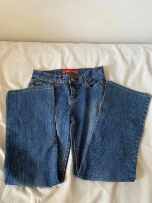 Blå bootcut jeans med raka ben vintage gina - Säljer ett par klassiska blå jeans med bootcut och raka ben. Jeansen har fem fickor, bälteshällor och kontrastsömmar. Materialet är kraftig denim i bomull och passformen är avslappnad med lite utsvängda ben. Perfekta till en avslappnad streetstyle-look.