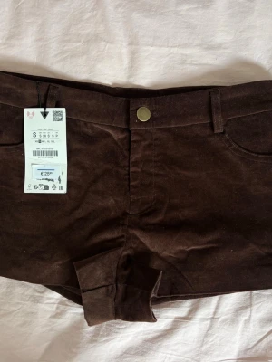 Bruna manchester shorts med uppvik - Snygga bruna shorts i mjuk manchester med uppvikta benslut och klassisk femficksdesign. Shortsen har bälteshällor och stängs med knapp och dragkedja. Perfekta för dig som vill ha en chill och trendig look till sommaren. Använt i typ fem timmar!!