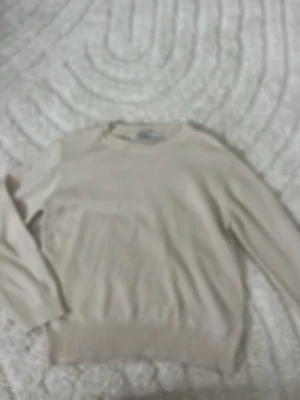 Beige stickad tröja från Zara - Säljer en stilren beige stickad tröja från Zara i storlek L. Tröjan har rund halsringning, långa ärmar och ribbade muddar vid ärmslut och nederkant. Perfekt för lager på lager och enkel att matcha med olika outfits.