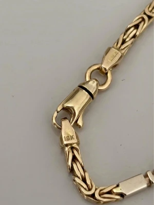 Guldarmband 18K flätad kedja - Snyggt armband i 18 karat guld med flätad kedjedesign och robust karbinlås. Armbandet har en klassisk guldfärg och passar perfekt för dig som gillar stilrena accessoarer. Märkt med 18K på låset.