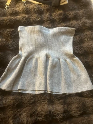Ljusgrå ribbad stickad kjol - Säljer en ljusgrå ribbad stickad kjol med peplumvolang nedtill. Kjolen har en tight passform upptill som ger en snygg siluett. Perfekt att styla med jeans eller kjol för en trendig look. Sydde om en tröja till denna kjol så den är inte helt perfekt.