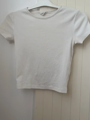Vit basic t-shirt i bomull - En enkel och stilren vit t-shirt med rund hals och korta ärmar. Tillverkad i mjuk bomull som känns skön mot huden. Perfekt att matcha med jeans eller shorts för en clean look.