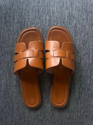 Bruna slip-in sandaler i läderimitation - Säljer ett par stilrena sandaler i en varm brun färg. Sandalerna är endast använda en gång så i jättebra skick. Säljer då de tyvärr var för stora. Storlek 40 och från Nelly!💗💗
