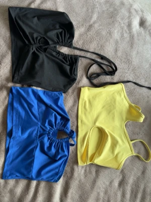 3 fina toppar - Säljer tre bandeau toppar i svart, blått och gult. Säljer alla 3 topparna tillsammans för 50kr. Det är storlek Xs men passar även Xxs. Alla har en snygg cut-out detalj framtill.  Perfekt för sommaren och att styla med  jeans eller kjol.