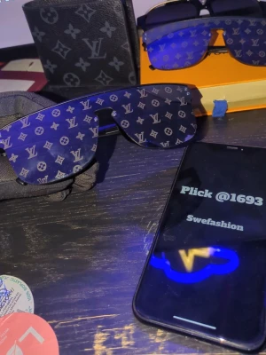  solglasögon - Säljer ett par solglasögn med det ikoniska L mönstret över hela glaset. Sköldformade linser och modern design som sticker ut. Perfekta för dig som vill ha en exklusiv accessoar med lyxig känsla.