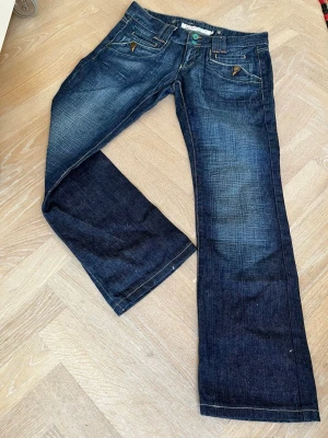 Lowrise jeans  - Jeans med låg midja från ICHI. Mörk wash. Turkosa knappar fram och gul brodyr bak. Storlek 30.