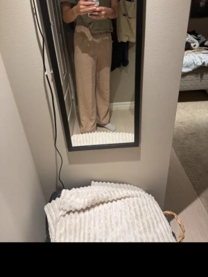 Beige vida kostymbyxor - Säljer ett par beige kostymbyxor med hög midja och vida ben. Byxorna har pressveck framtill, bälteshällor och stängs med hake och dragkedja. Perfekta för en clean och stilren look.