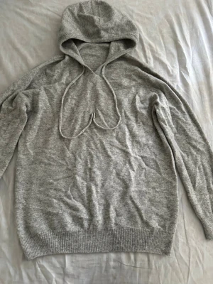 Kashmir stickad hoodie  - En enkel och stilren ljusgrå hoodie med huva och dragsko. Tillverkad i mjukt stickat material och har ribbade muddar vid ärmslut och nederkant. Perfekt för en avslappnad look.