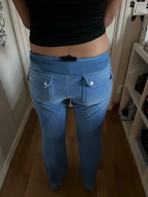 Blå juicy byxor  - Xs men passar även S och M.Säljer ett par blå mjukisbyxor i mjukt velourmaterial. Byxorna har två bakfickor med knappdetaljer och broderad logga ovanför ena fickan. Perfekta för chill dagar hemma eller när du vill vara extra bekväm.