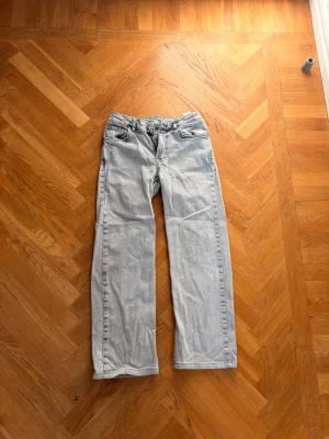 Gråa raka jeans - Säljer ett par gråa jeans med rak passform och klassisk femficksdesign. Jeansen har bälteshällor och knappgylf. Materialet är denim i bomull och färgen är tvättad ljusblå, perfekt för en avslappnad stil.