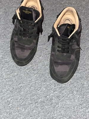 Svarta Valentino rockrunners med nitar - Snygga svarta sneakers från Valentino med coola nitar på hälen och svart kamouflagemönster👌🏼. Skorna har svarta skosnören, beige insida och detaljer i mocka och textil. Perfekta för dig som vill ha något unikt och trendigt🔥🔥. Släppt litegran på höger sula men kan lagas hos en skomakare utan problem . Packeteras ordentligt vid frakt!! 📦🚛