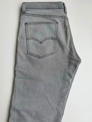 Grå raka jeans med kontrastsömmar - Snygga grå jeans med raka ben och tydliga kontrastsömmar på bakfickorna. Klassisk femficksmodell i mjukt denimtyg. Passar perfekt till en avslappnad streetwear-look och är lätta att matcha med olika stilar.