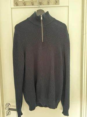 Zara quarterzip  - Mörkblå stickad tröja med hög krage och halvzip framtill. Tröjan har ribbstickad struktur, långa ärmar och en avslappnad passform. Perfekt för lager på lager och enkel att styla till olika outfits.