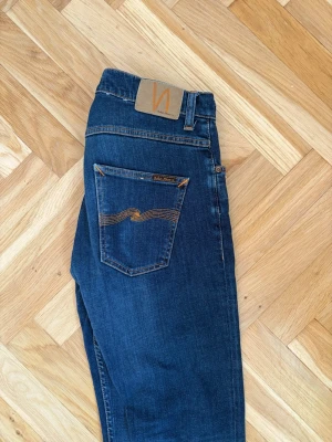 Mörkblå jeans från Nudie Jeans - Snygga mörkblå jeans från Nudie Jeans med klassisk femficksmodell och kontrastsömmar. Jeansen har en smal passform och är tillverkade i mjuk bomull. Perfekta för dig som gillar stilrena och tidlösa jeans.