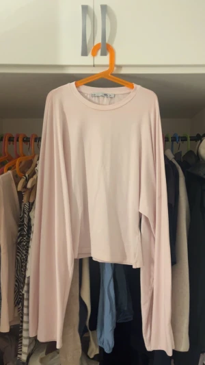 Ljusrosa långärmad topp 157 - En enkel och stilren ljusrosa långärmad topp från 157. Modellen har rund halsringning och är tillverkad i mjuk bomull, perfekt för en avslappnad look. Passformen är loose och toppen är något croppad vilket ger en trendig vibe.