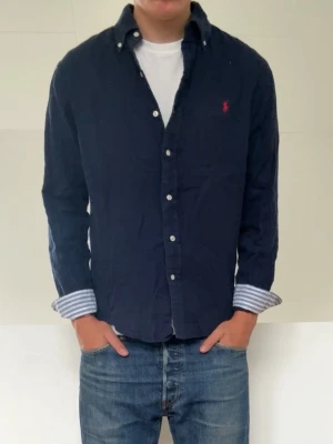 Mörkblå Randig Ralph Lauren skjorta - Mörkblå Ralph Lauren skjorta med randiga ärmar i strl M men sitter som en S! Skjortan har en defekt på sista bilden då den har ett hål/öppning på ena ärmen men går att laga om man vill eller så syns d inte ifall ärmen är uppkavlad! 